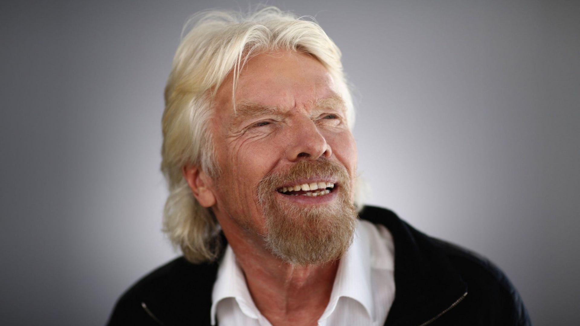 Richard Branson Smiling And Wearing Black Over A White Shirt