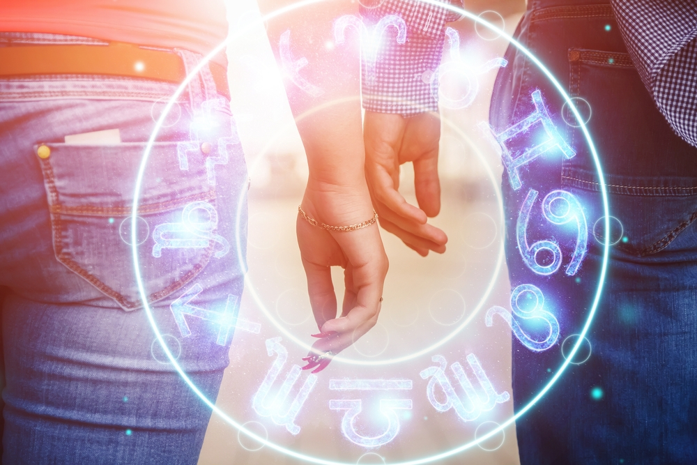 A man and a woman's hand almost touching and a zodiac wheel hologram in the center.