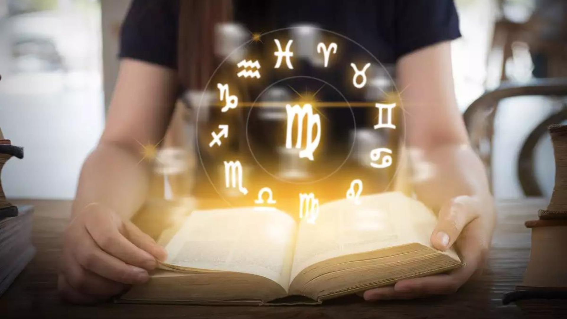 A person with an open book and a hologram of zodiac signs on a wheel.
