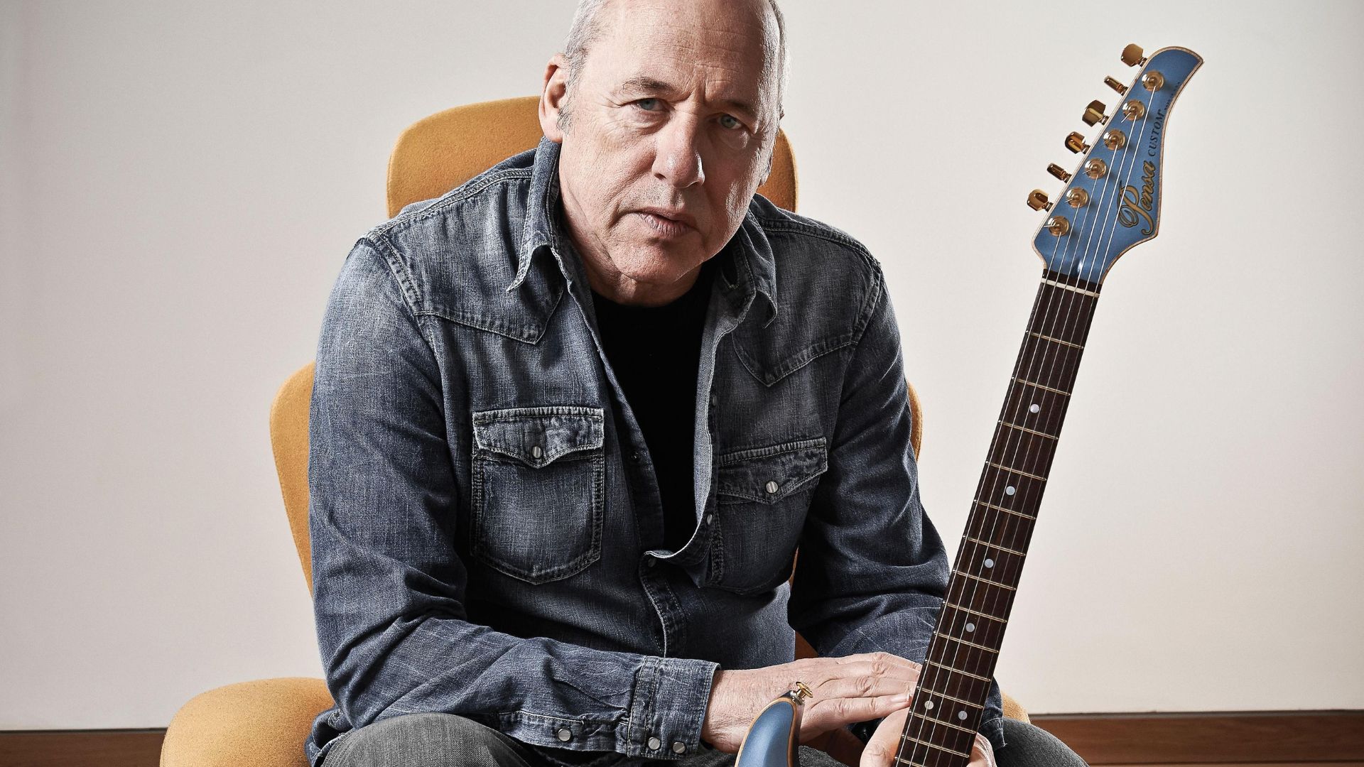 Mark Knopfler Sitting On A Chair Holding Guitar