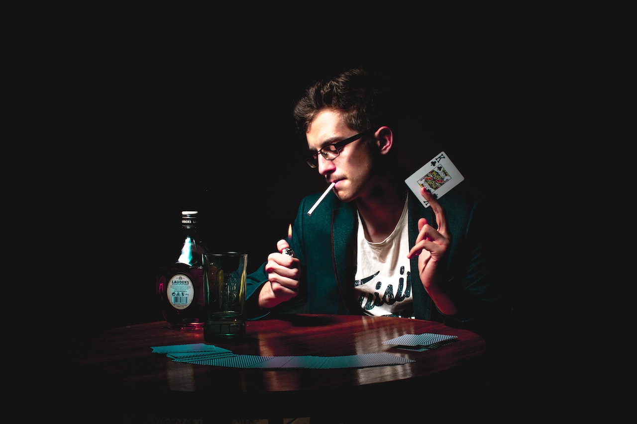 A Magician Holding A Playing Card While He Smokes