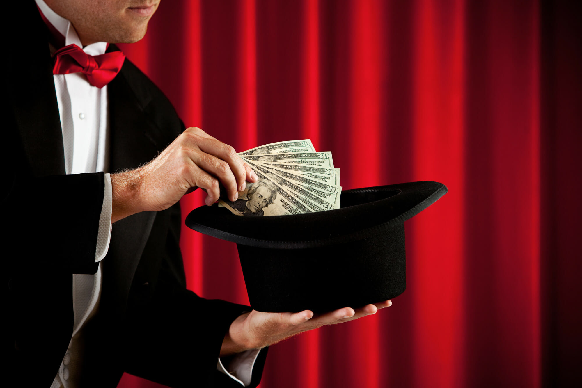 A Magician Holding Dollar Bills Over A Black Hat