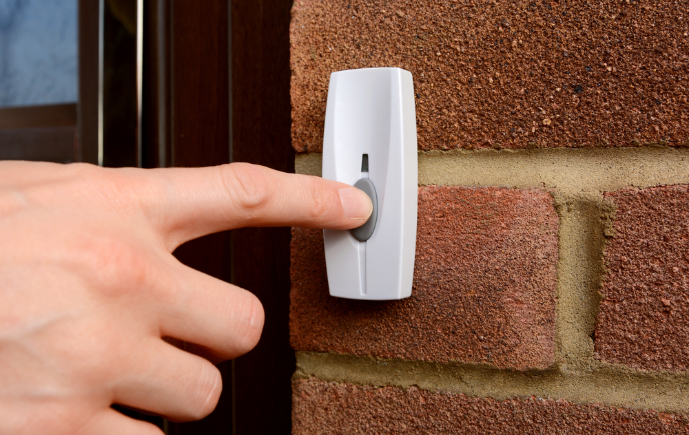 A hand pressing a doorbell button.