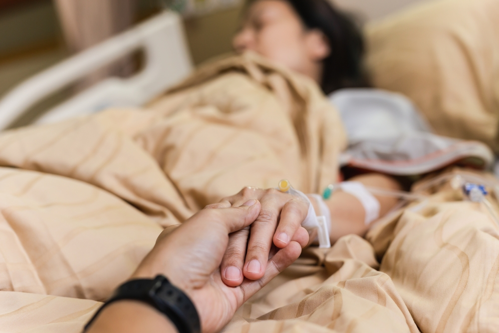 Husband hand holding his wife hand on bed in hospital room