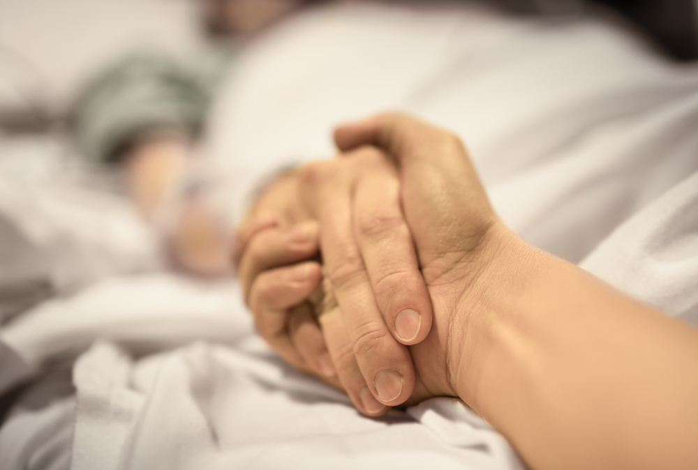Man holding hand, giving support and comfort to woman, loved one sick in hospital bed