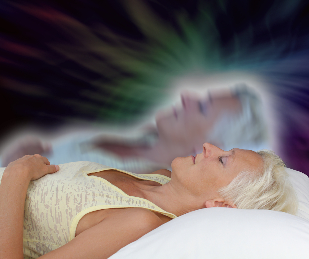 Female lying supine with eyes closed experiencing astral projection on dark background