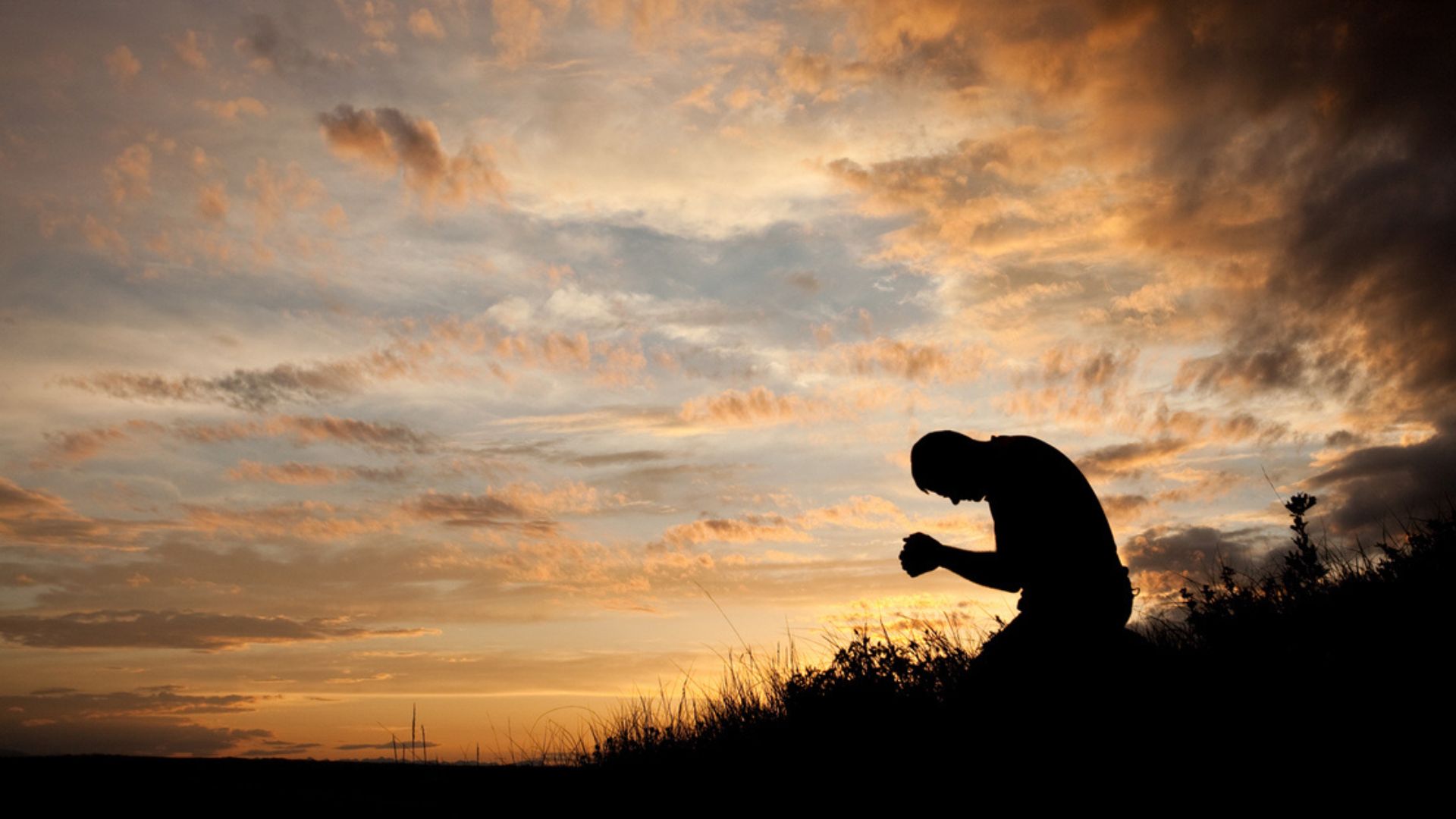 A Man Sitting And Praying On Grass Field