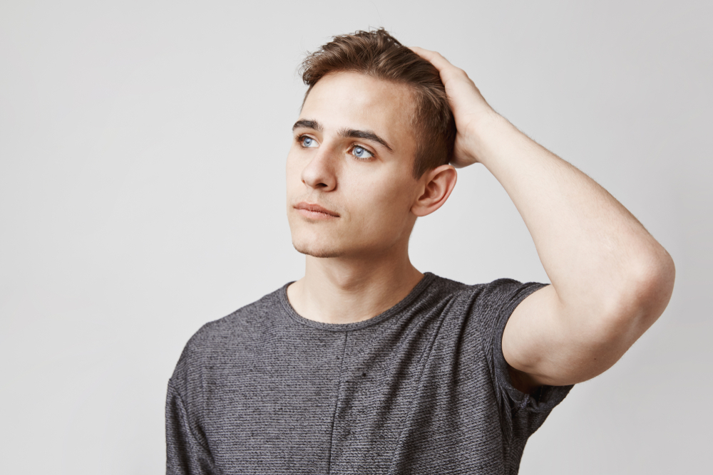 Portrait of young man with beautiful blue eyes touching his head