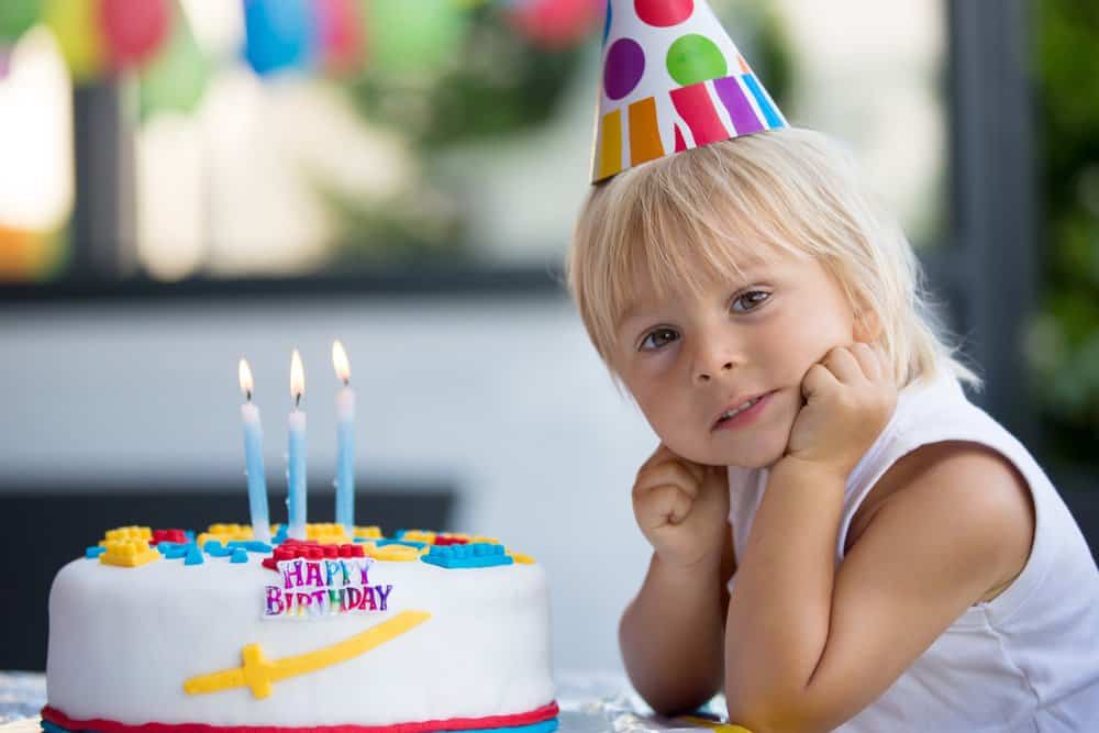 Little Boy with Party Hat Sitting Beside His Birthday Cake