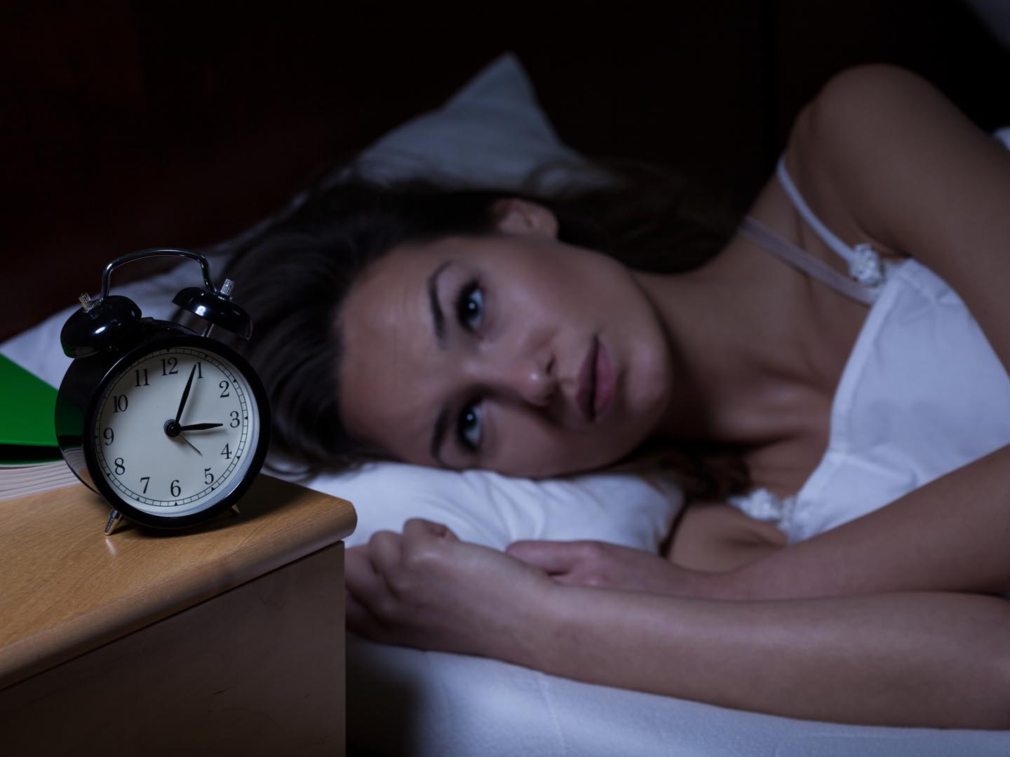 A Woman Laying On Bed Setting Alarm On Clock