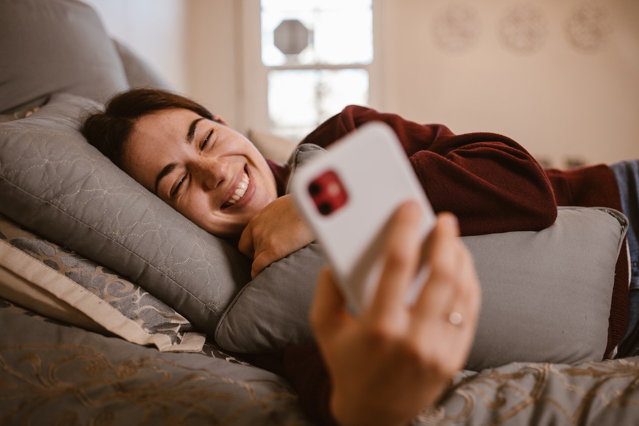 A Woman Using Her Smartphone while Lying Down in Bed