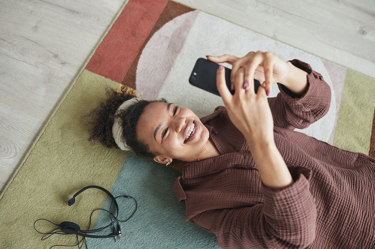 A Happy Woman Using Her Smartphone while Lying Down on the Rug