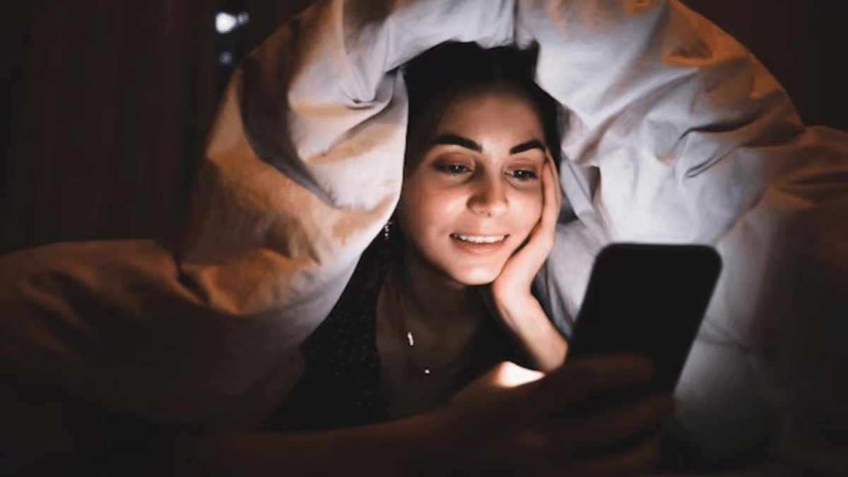 A Woman Smiling While Using a Smartphone in Bed