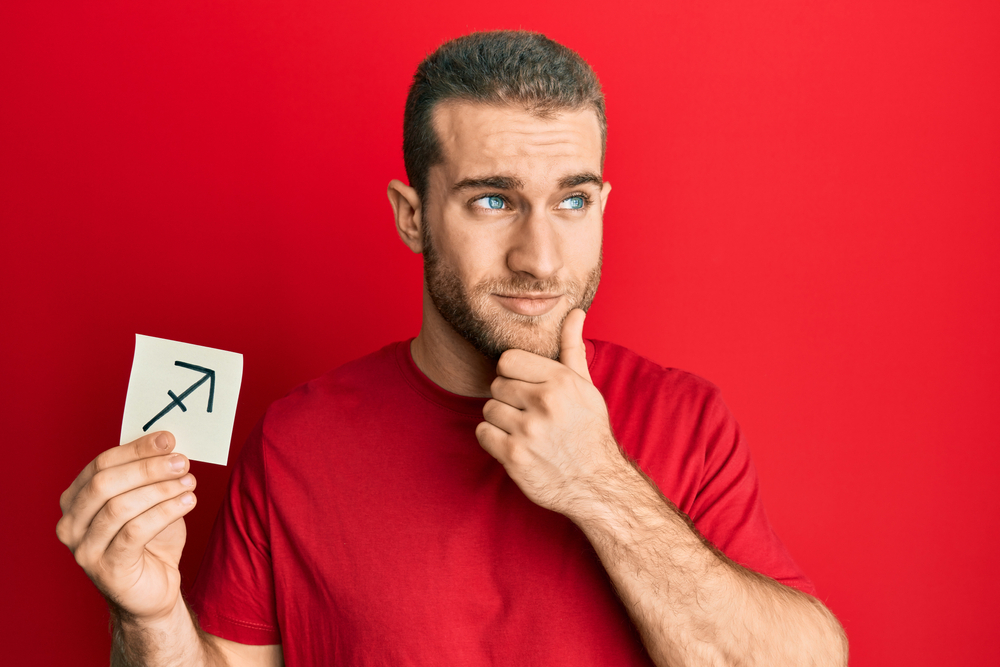 Man in red holding a paper with sagittarius zodiac sign.