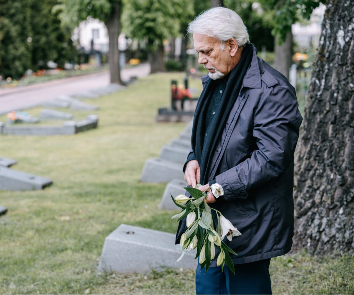 An Old Man Holding Flowers in a Graveyard