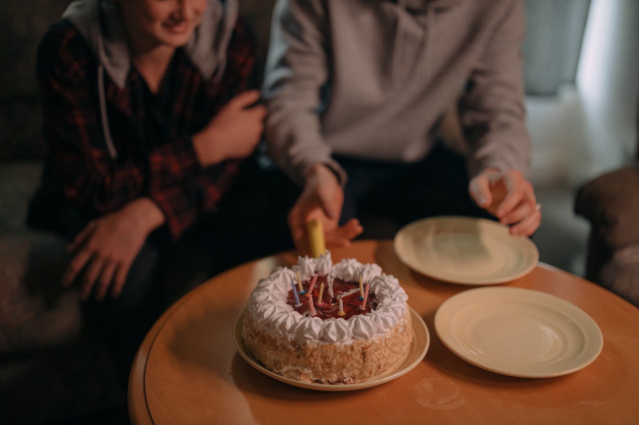 People Sitting at a Table with Birthday Cake and Plates