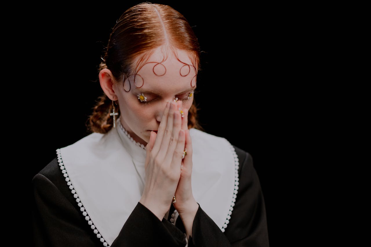 A Woman in Black Long Sleeves Praying Solemnly